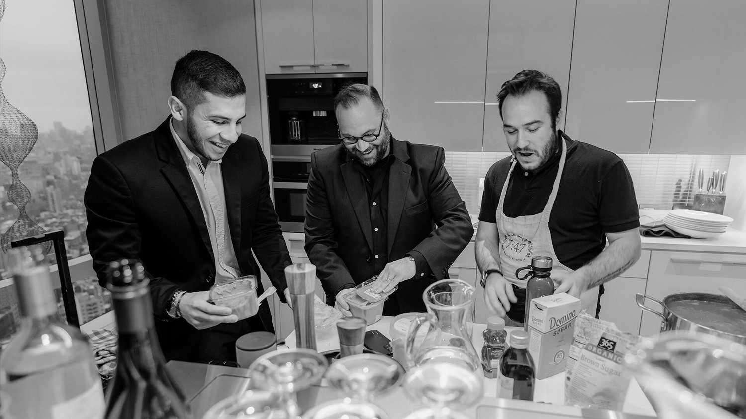 Three people cooking and laughing together around a kitchen island